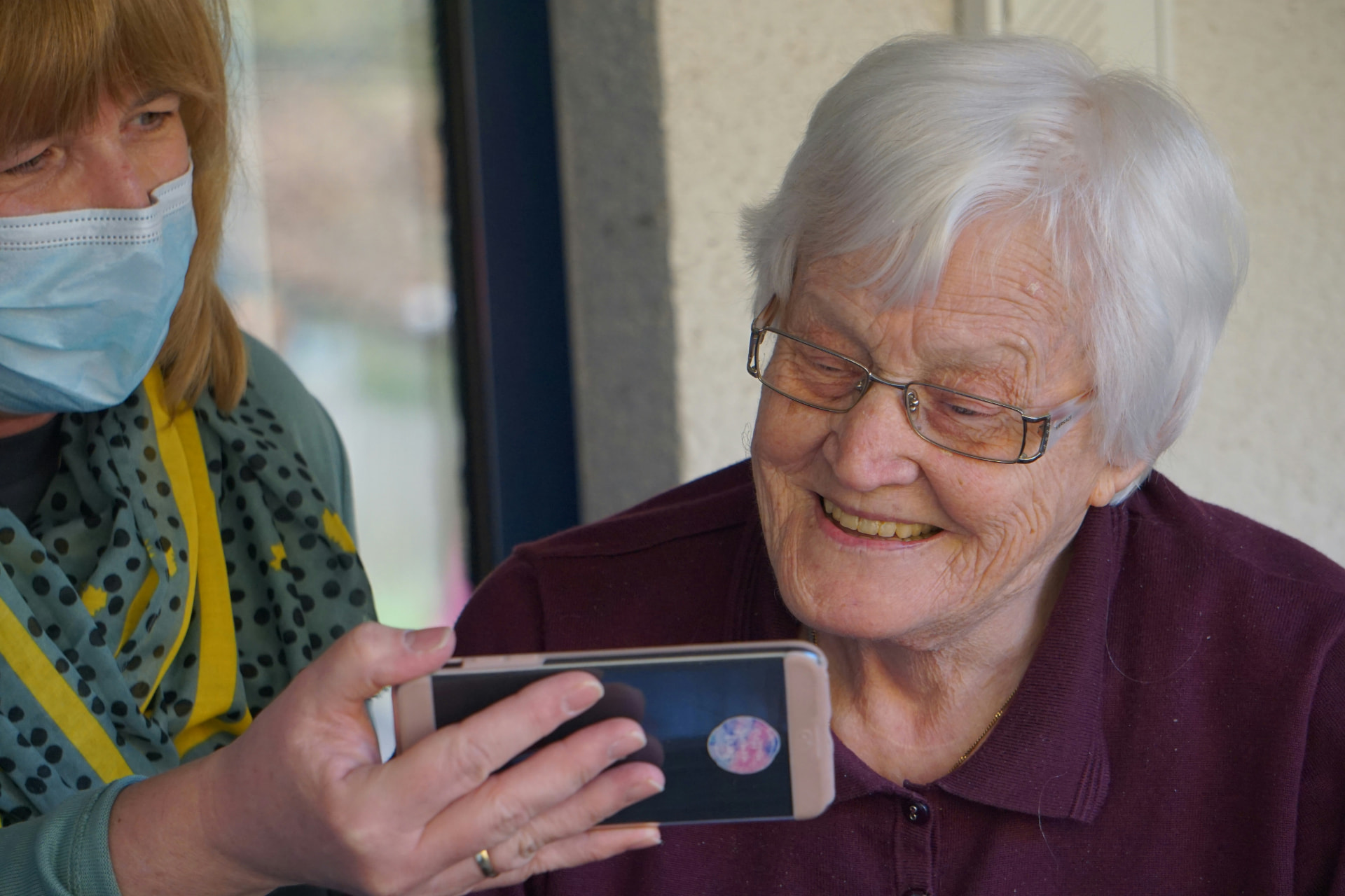 Ältere Dame telefoniert lächelnd mit Unterstützung einer Betreuerin